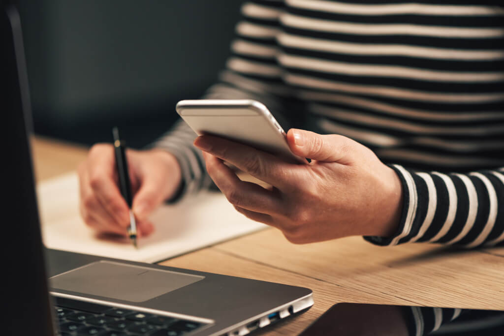 woman checking smartphone and taking notes